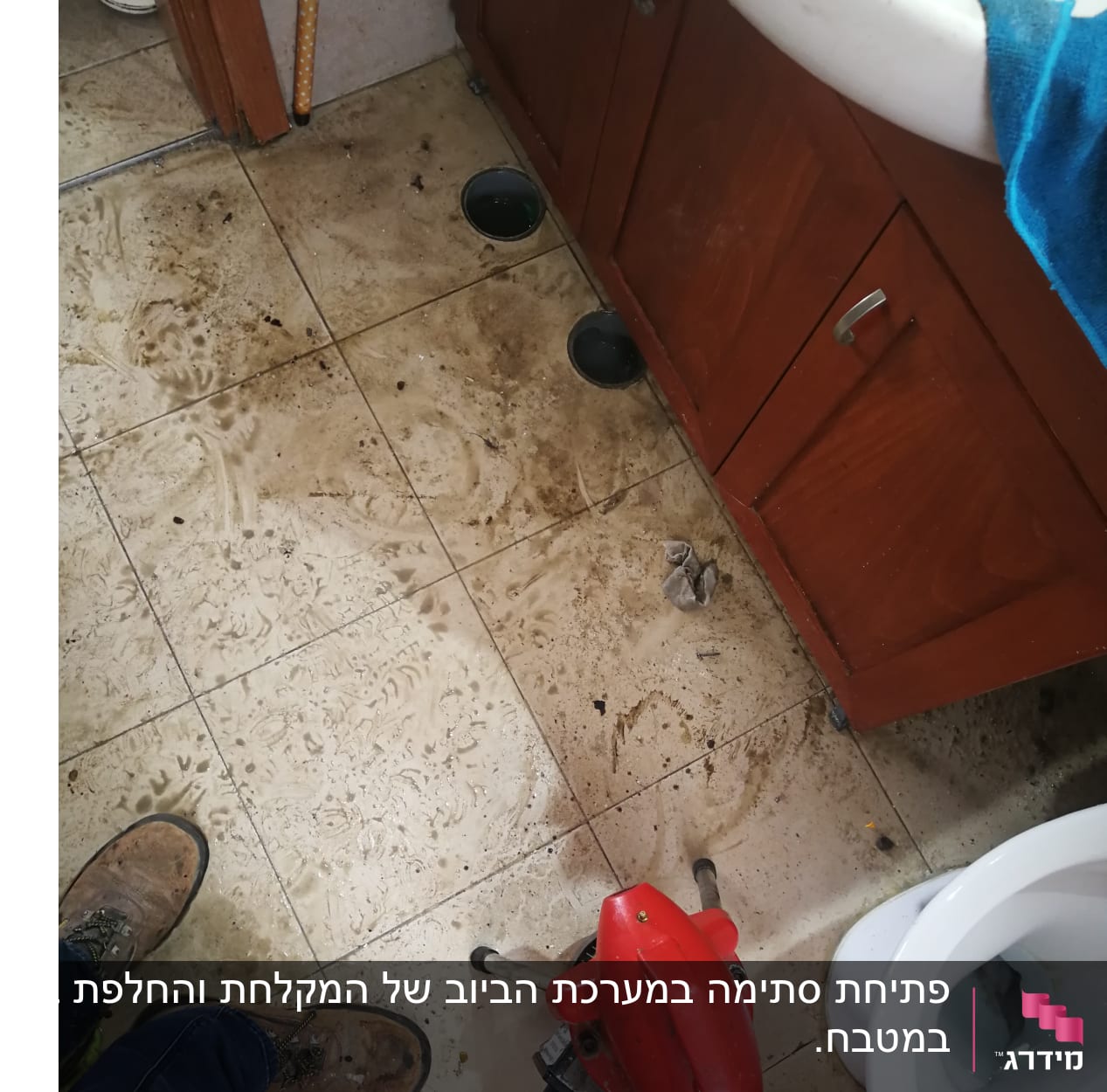 כלי עבודה אדום על רצפה מלוכלכת ליד כיור ושירותים